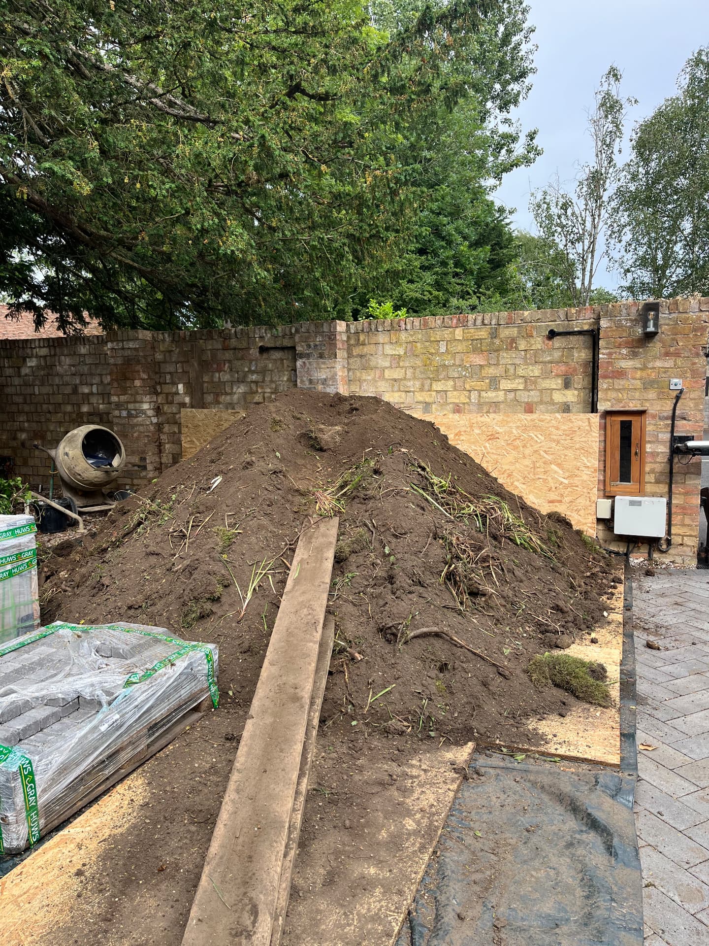 Excavated soil stacked on boards beside the brick wall in Godmanchester