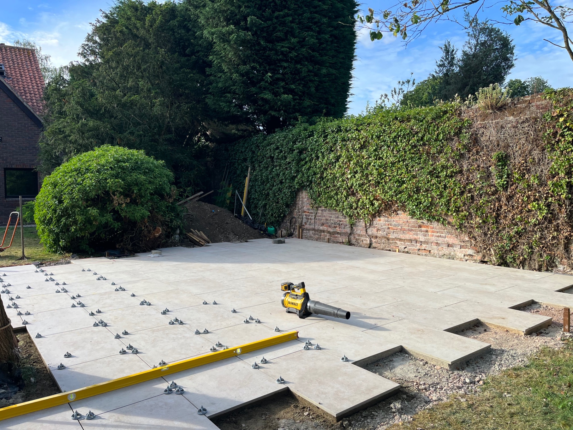 Porcelain patio nearing completion beside the ivy-covered brick wall in Godmanchester
