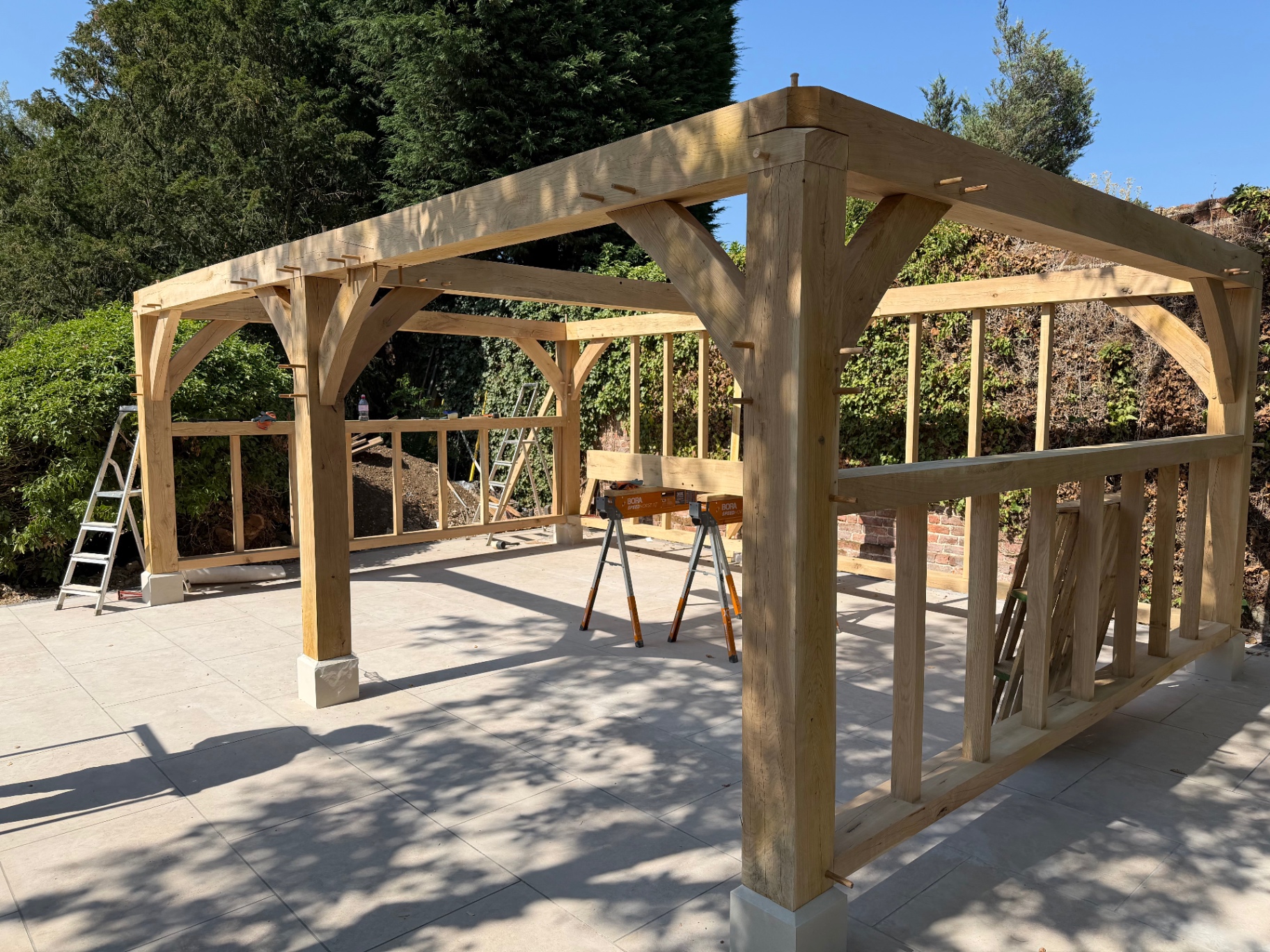 Oak gazebo frame with curved braces and balustrade panels on the porcelain patio in Godmanchester, Cambridgeshire