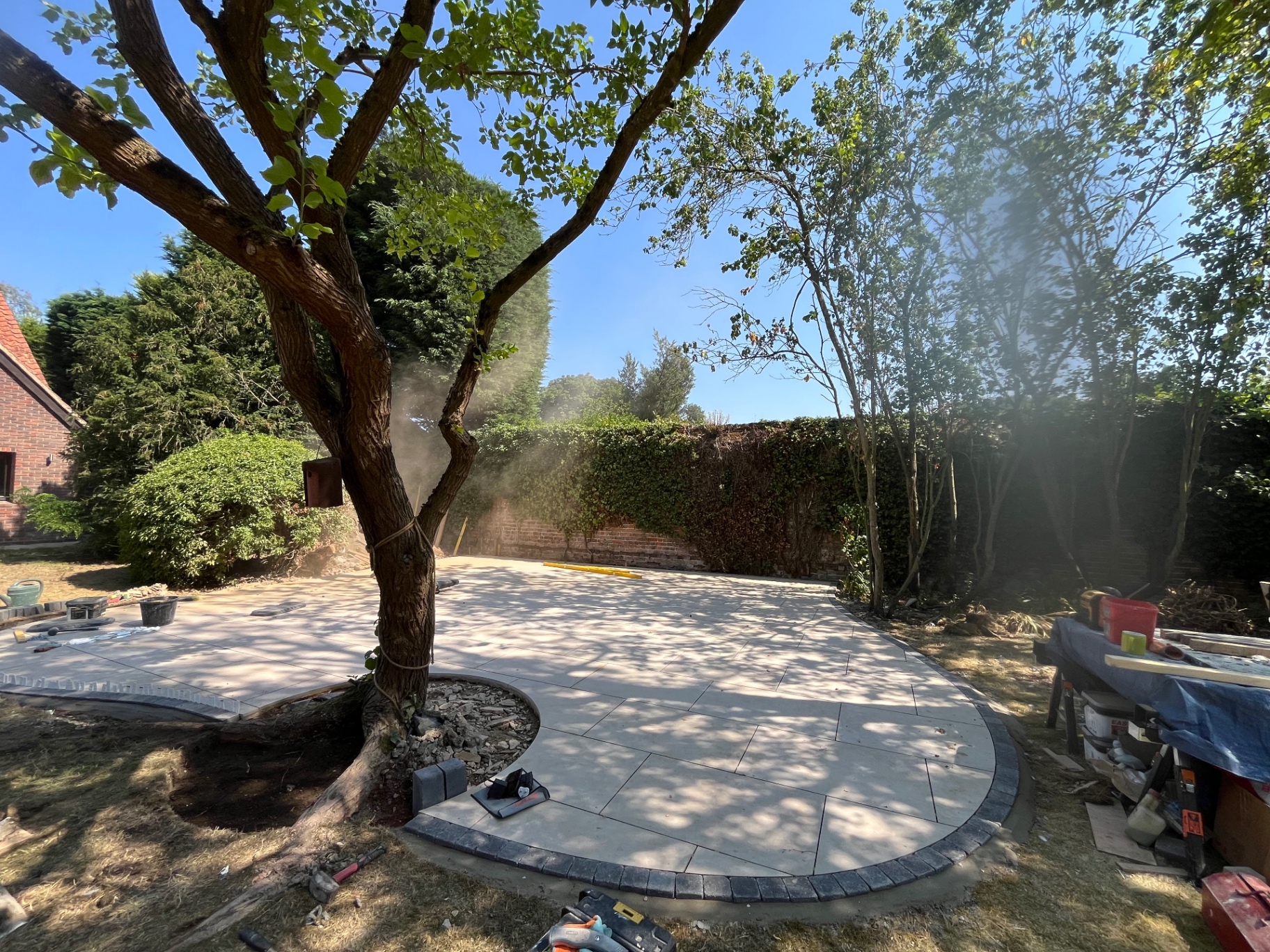 Curved porcelain patio laid around a mature tree with sett border in Godmanchester, Cambridgeshire