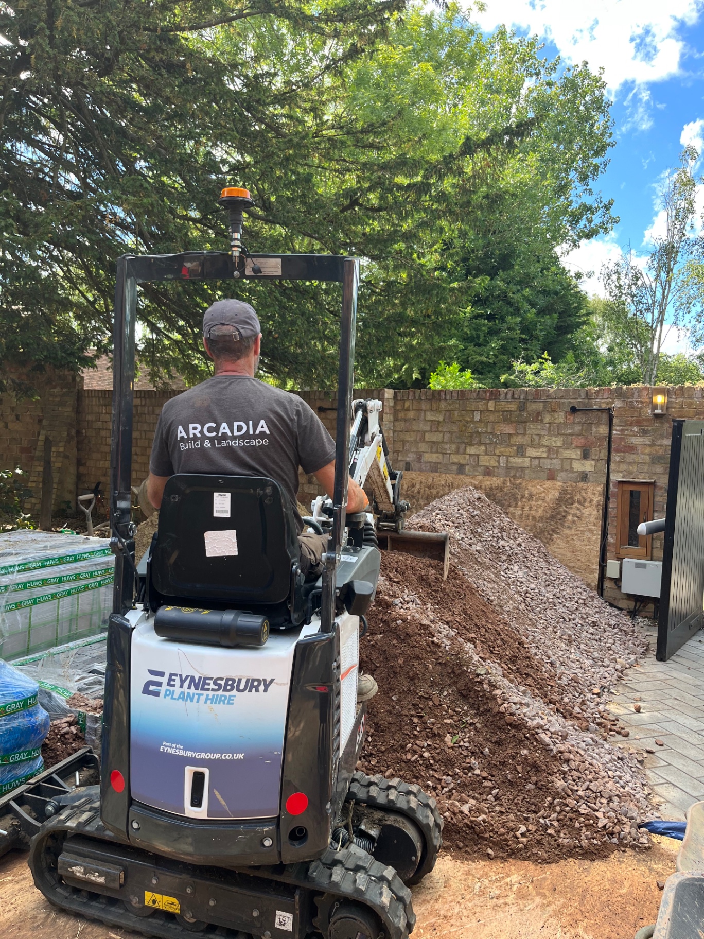 Arcadia Build and Landscape team member operating a mini digger moving aggregate in Godmanchester