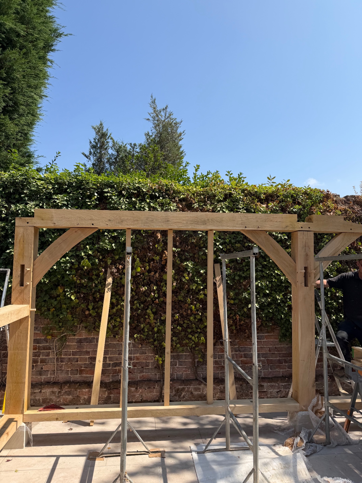 Oak gazebo beam and curved braces lifted into place against the brick wall in Godmanchester