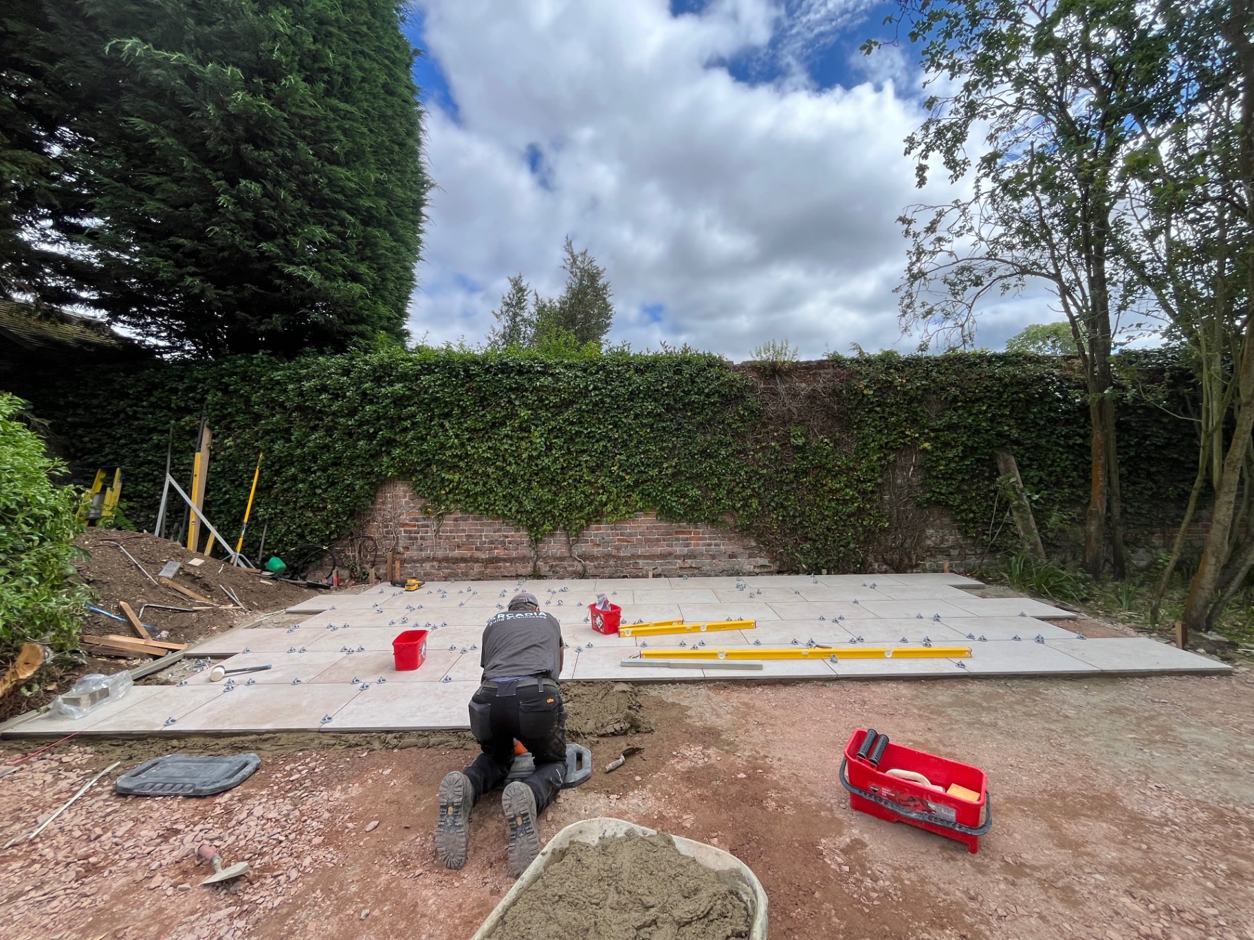 Landscaper laying porcelain paving with levelling clips in front of the old brick wall in Godmanchester, Cambridgeshire