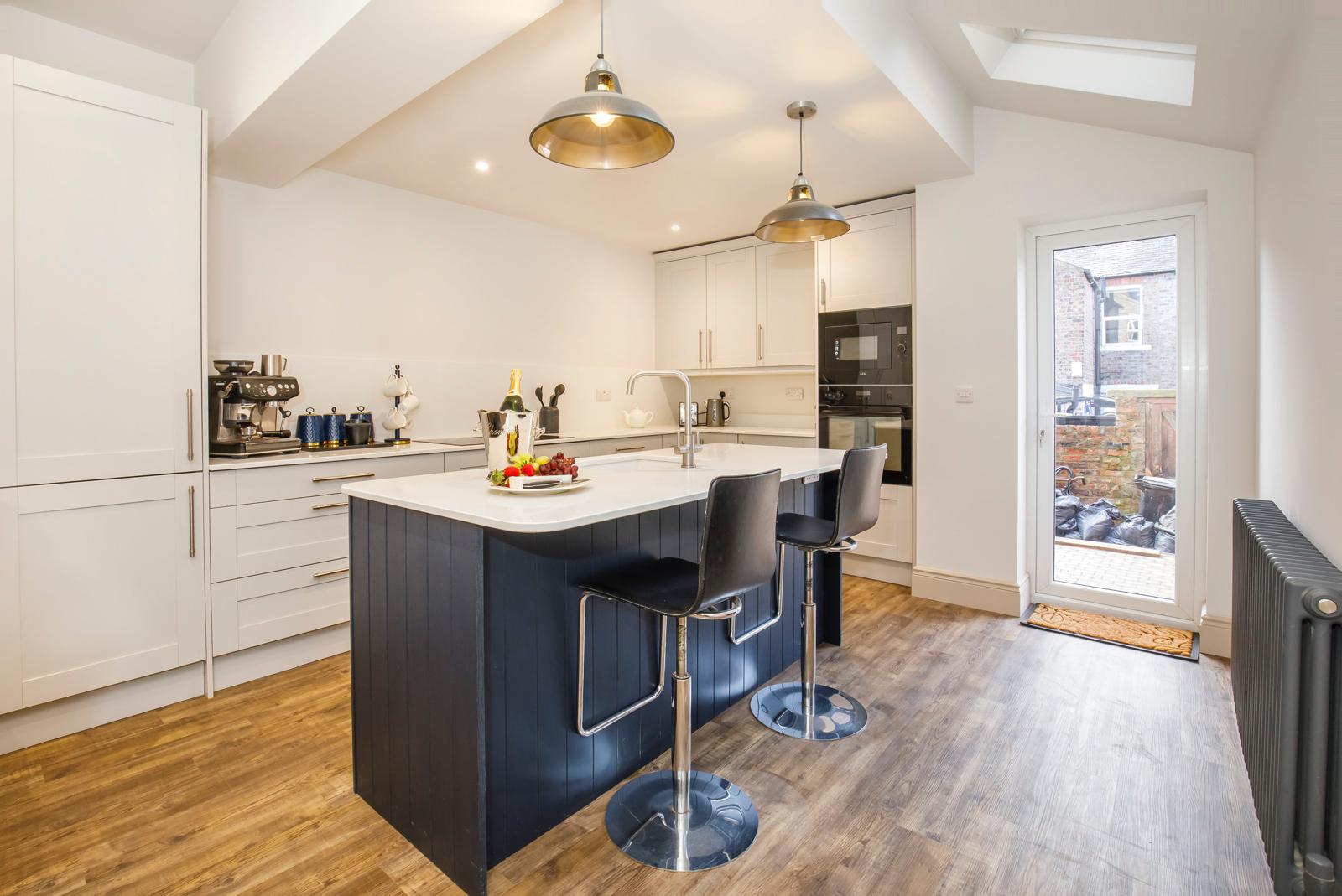 Finished kitchen with navy island, shaker units and pendant lights leading to rear door in Cambridgeshire