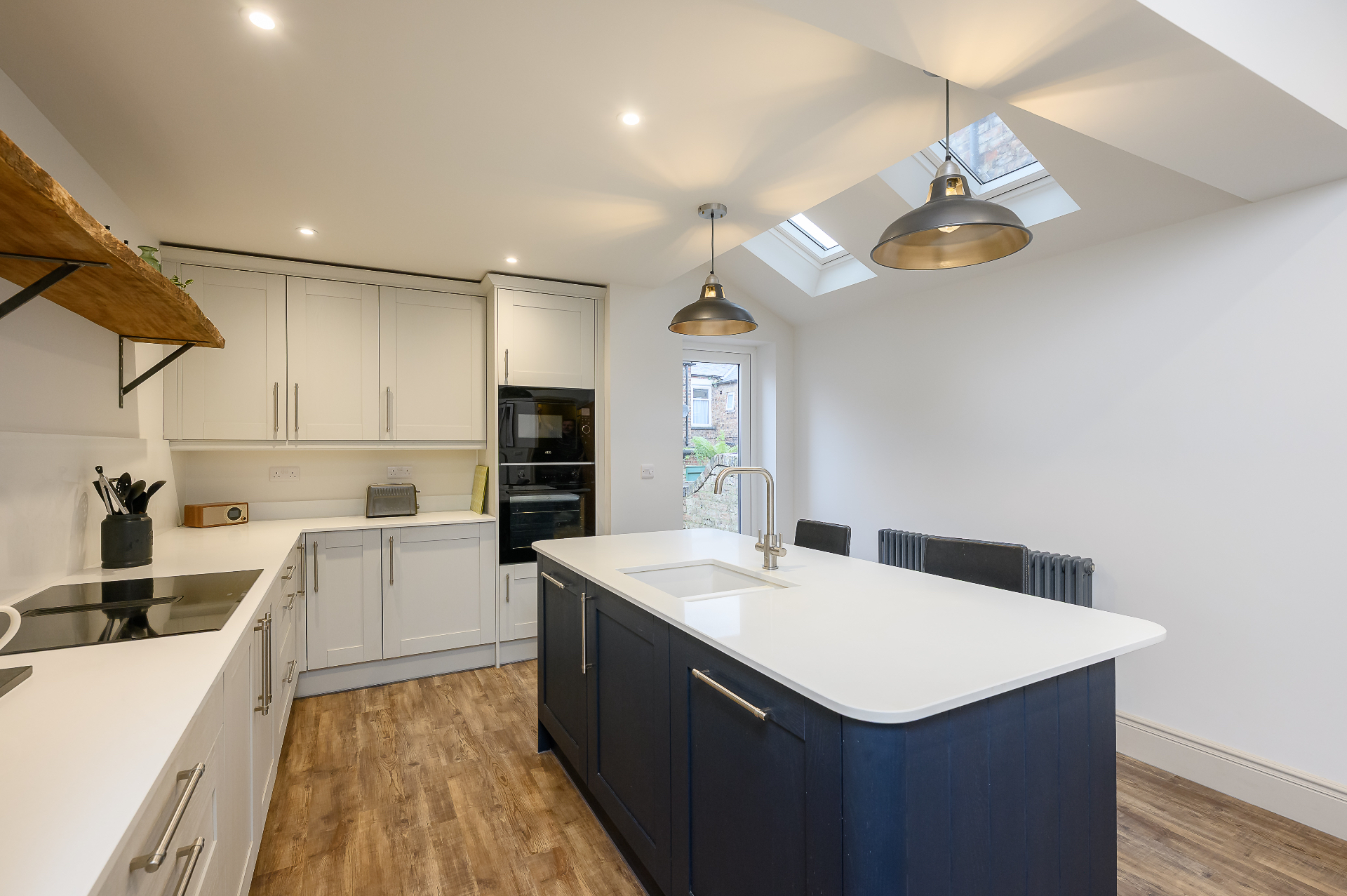 Open plan kitchen with navy island, twin Velux skylights and live-edge oak shelving in Cambridgeshire