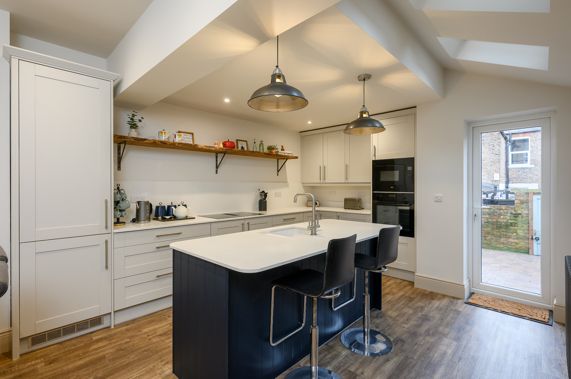 Wide view of finished open plan kitchen with navy island and rear door to garden in Cambridgeshire