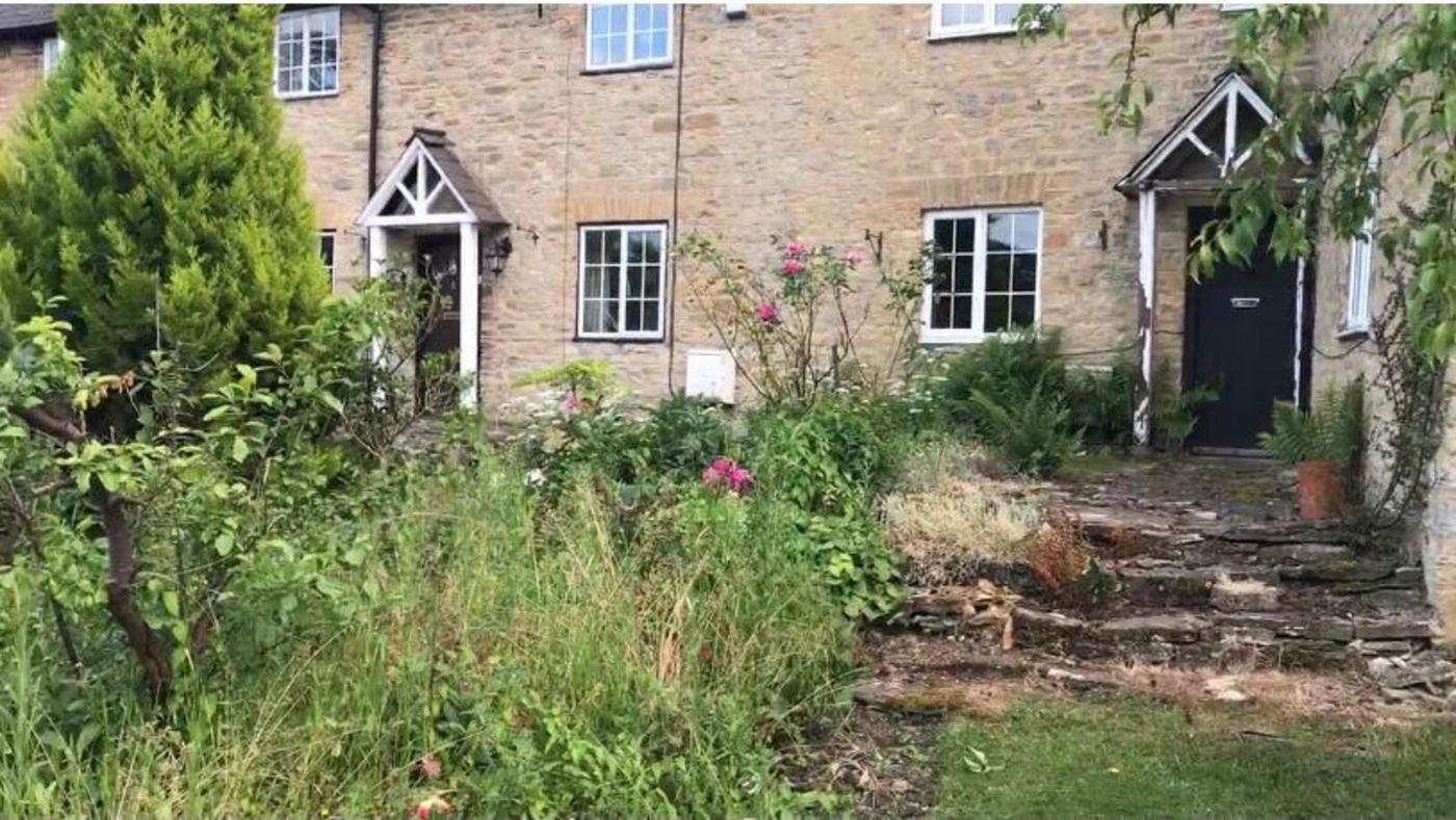 Front garden of the Turvey stone cottage before landscaping - overgrown beds and tired path by Arcadia Build & Landscape