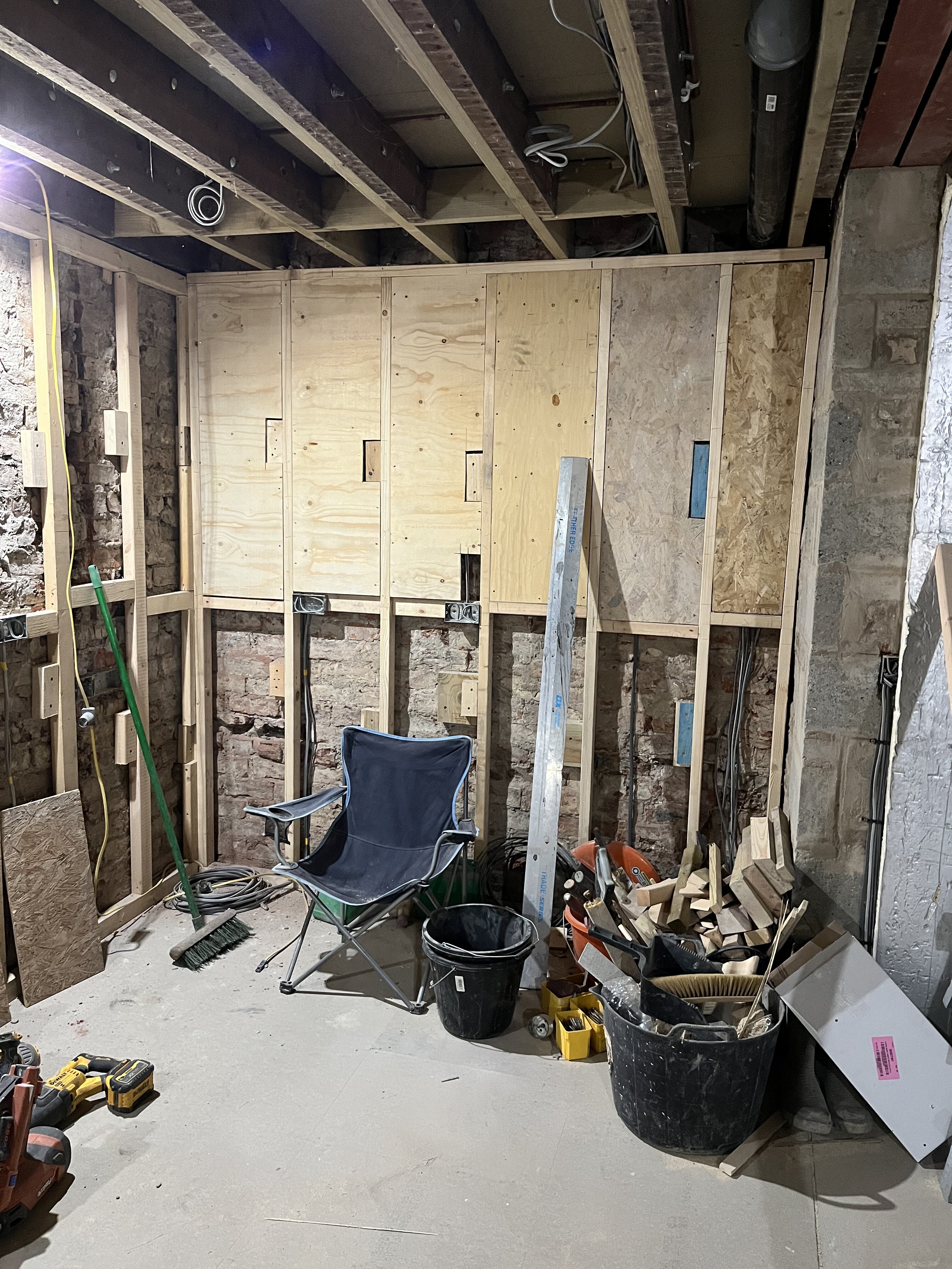 Plywood pads and stud framing on original brick wall during Cambridgeshire renovation