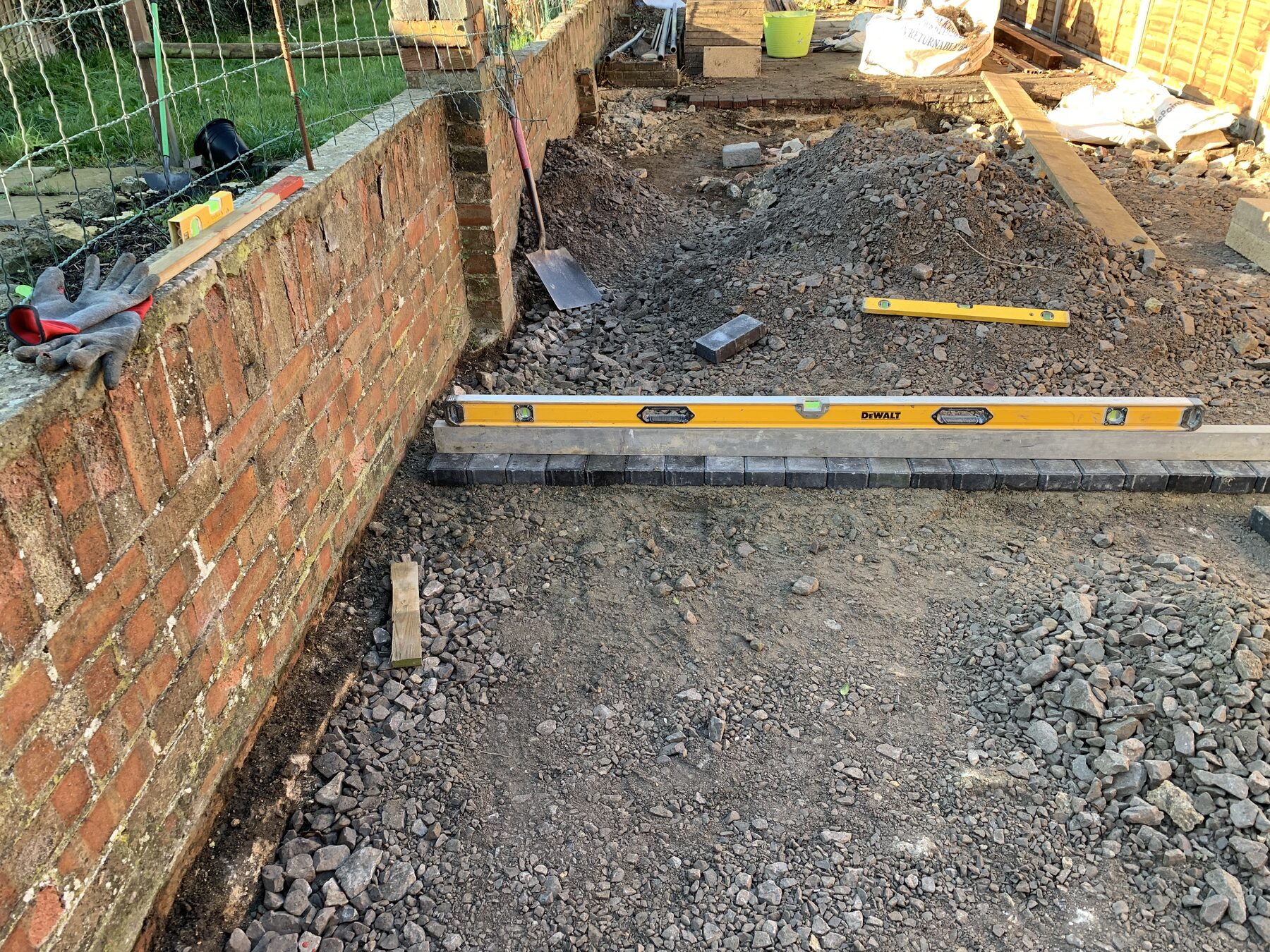 Charcoal block paving border being laid against brick wall in Fletton