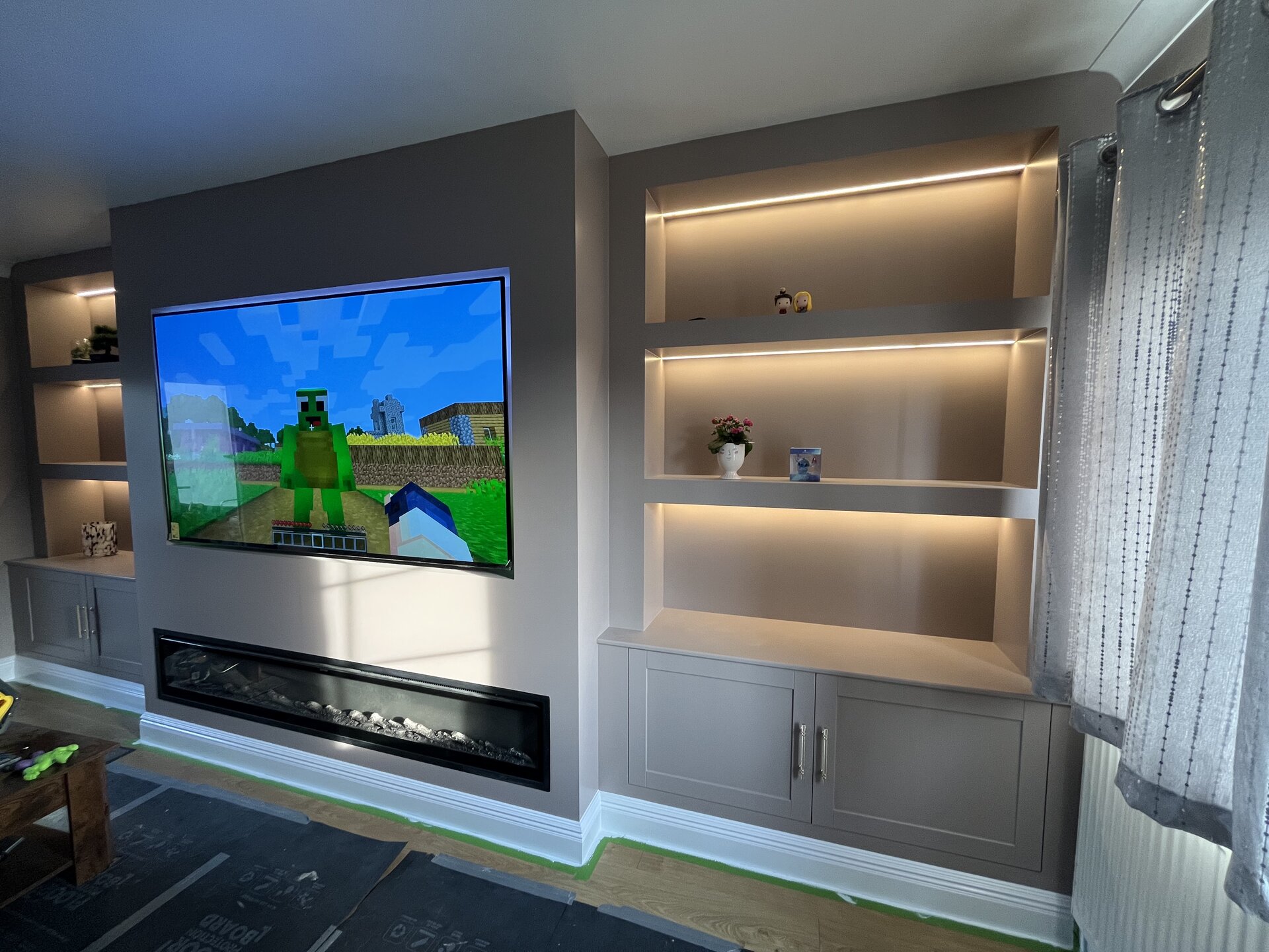 Completed media wall with TV in use and warm LED-lit alcove shelving in Sawtry living room