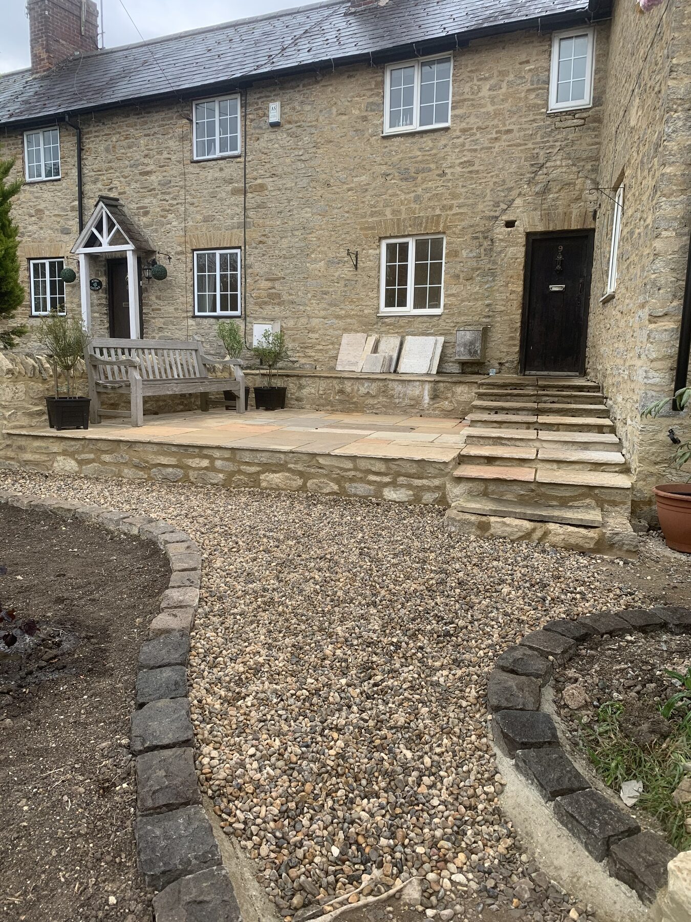 Front cottage with finished reclaimed sandstone patio, stone walls, cobble-edged gravel and bench in Turvey, Bedfordshire