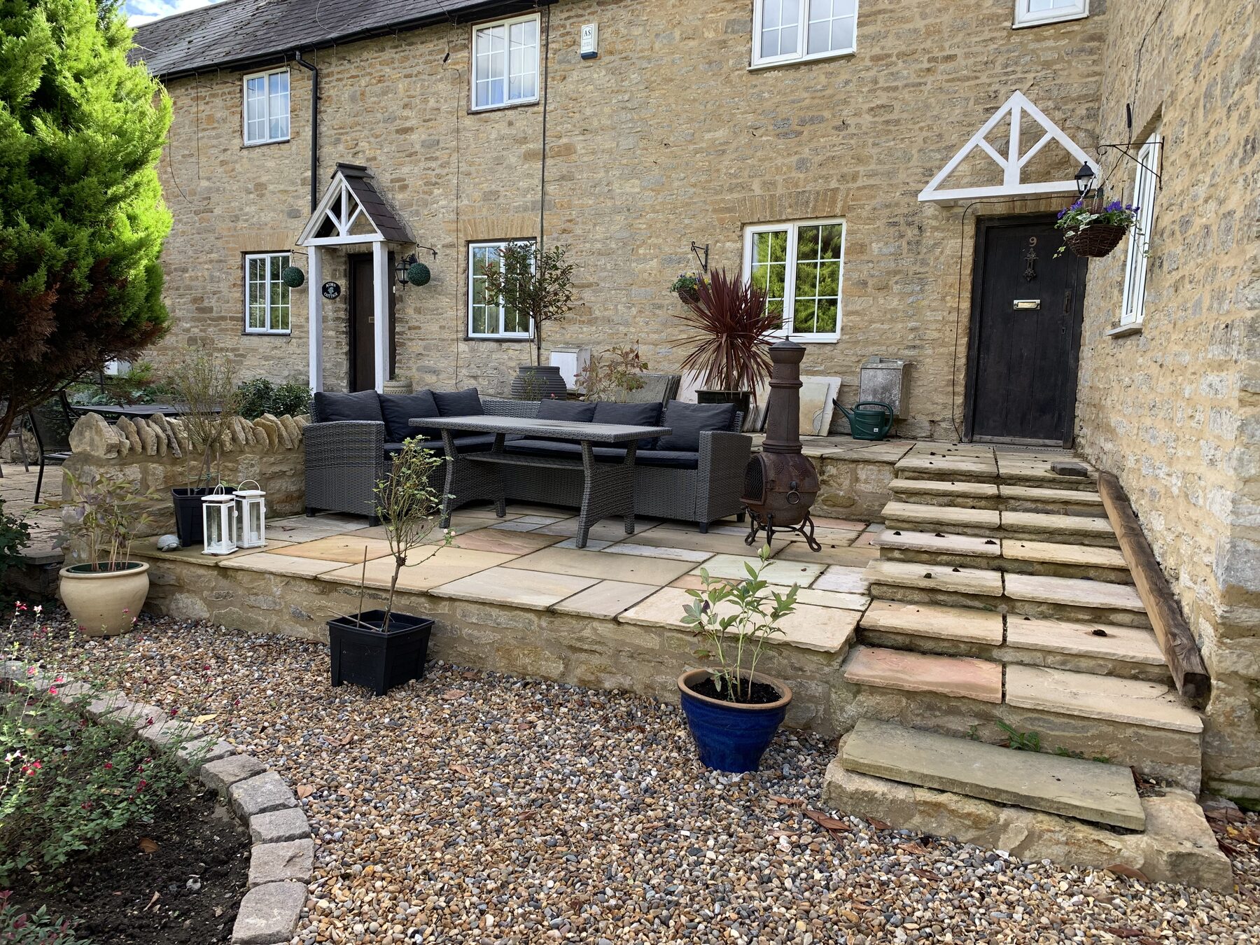 Finished reclaimed Indian sandstone patio with rattan sofa, chiminea and dressed cottage frontage in Turvey, Bedfordshire