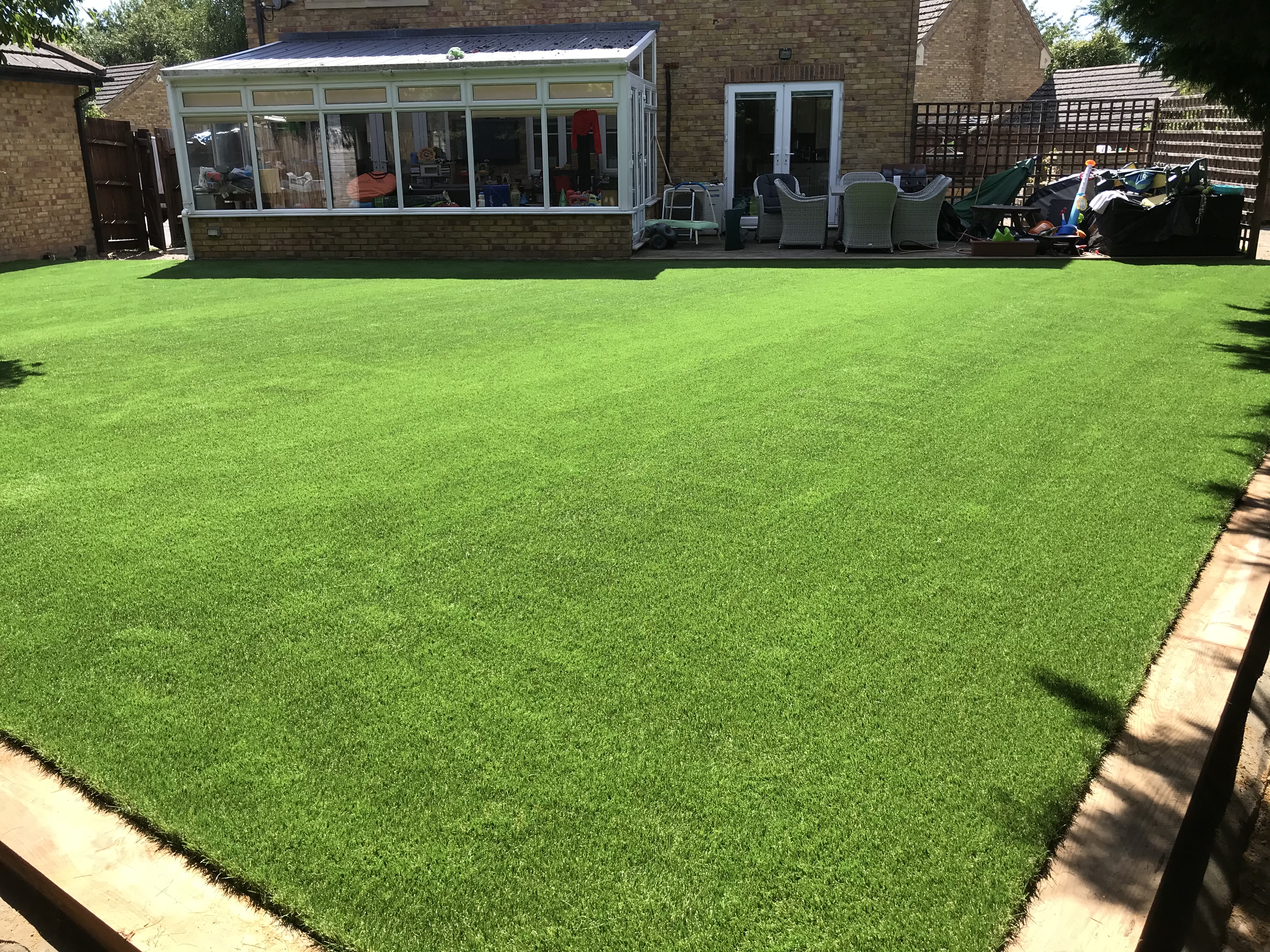 Premium artificial grass lawn installed alongside boundary trees in Turvey, Bedfordshire