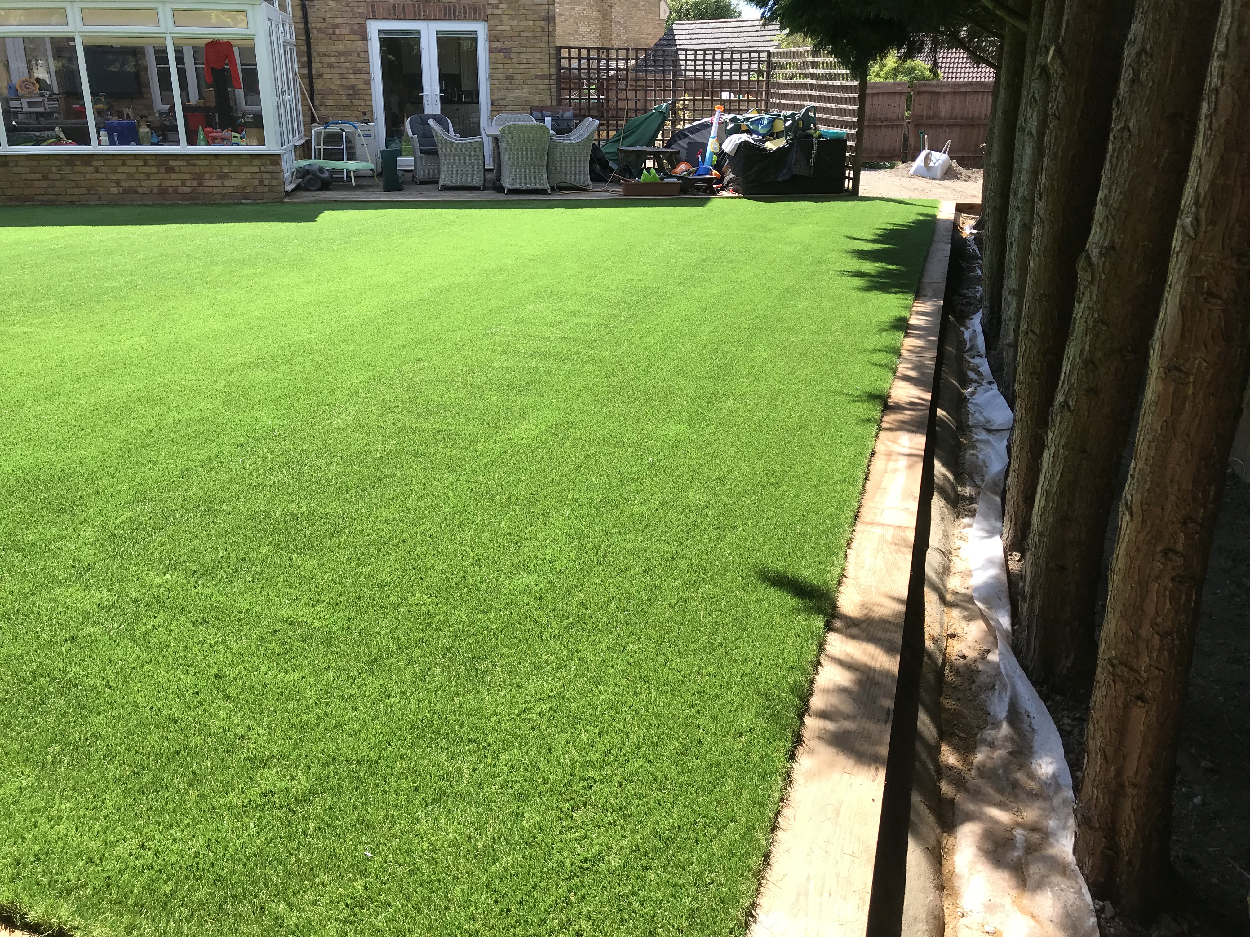 Wide view of finished artificial grass lawn looking back to conservatory in Turvey, Bedfordshire