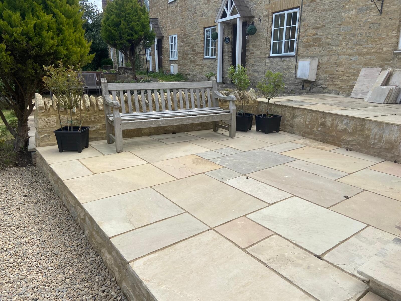Wide view of finished raised reclaimed sandstone patio, stone wall, bench and cottage frontage in Turvey, Bedfordshire