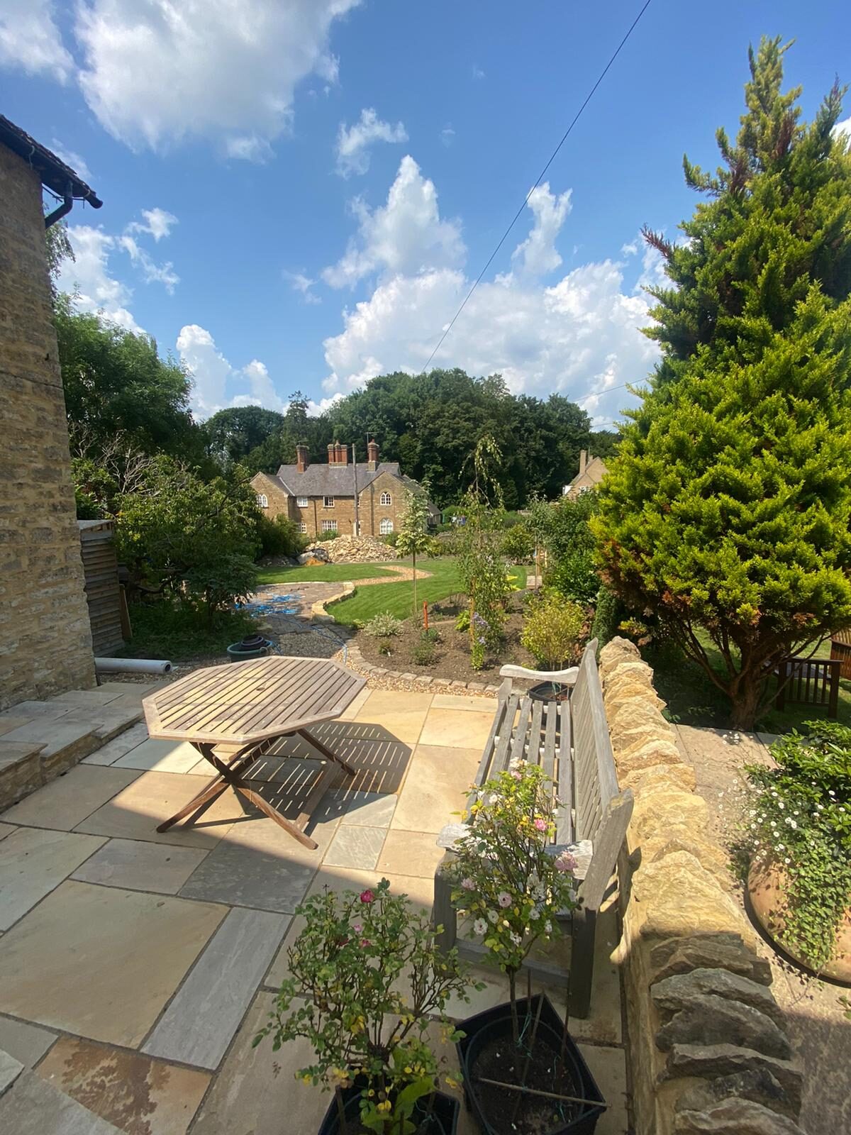 Sunny finished rear garden with sandstone patio, octagonal table, roses, lawn and cottage view in Turvey, Bedfordshire